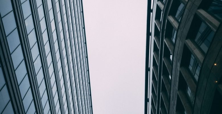 An upward vertical shot of modern tall business buildings with a white sky
